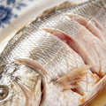 Raw whole sea bass with silvery skin and scored slits, close up